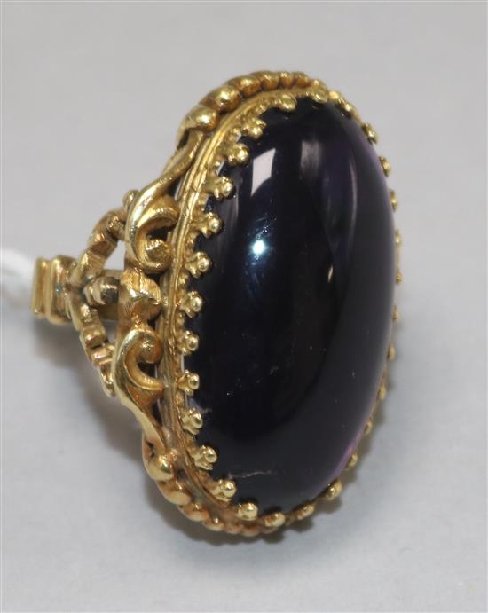 A large gold and cabochon amethyst set dress ring, with ornate carved shank and setting and pierced scroll shoulders, size J.